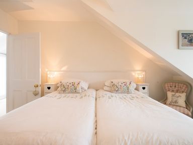 A bedroom with two single beds and floral pillows two bedside tables with lamps and an armchair with a cushion at Spiral View in Perranporth