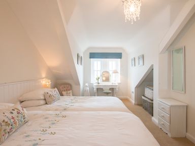 A bedroom with two beds a dressing table and a chair at Spiral View in Perranporth