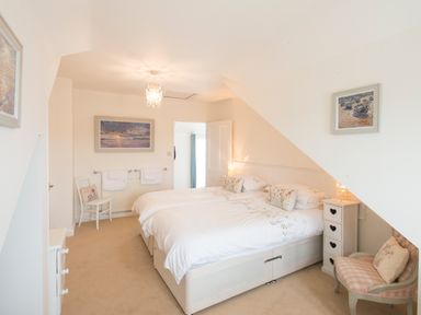 A bedroom with twin beds, a chair, bedside tables, and framed paintings at Spiral View in Perranporth