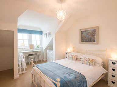 A bedroom with a double bed white furniture a desk and window with blue blinds at Spiral View in Perranporth