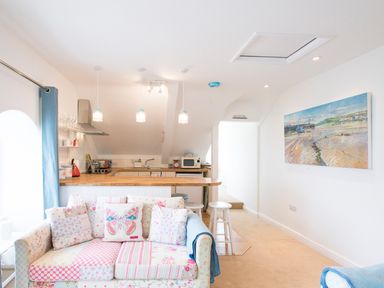 A kitchen with hanging lights and a wooden counter with stools and a floral sofa with butterfly cushion at Spiral View in Perranporth