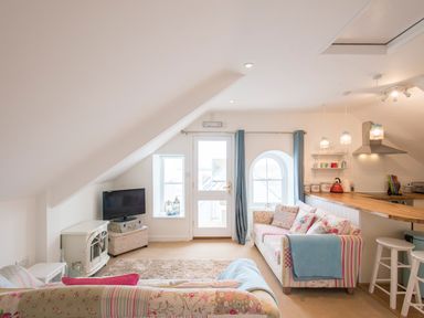 A living room with two patterned sofas a television and a kitchen area with wooden countertop at Spiral View in Perranporth