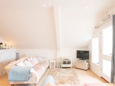 A bright living room with floral sofas a TV on a wicker chest a small white wood stove and a cabinet at Spiral View in Perranporth