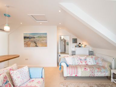 A living room with floral patterned sofas a wooden countertop and paintings on white walls at Spiral View in Perranporth