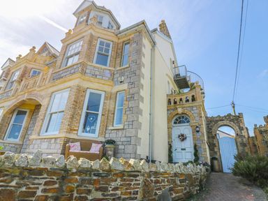 A stone and brick house with white windows a white door with a wreath and a stone wall at Spiral View in Perranporth