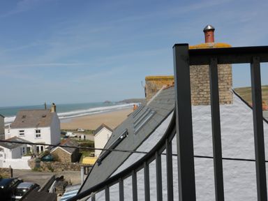 A coastal view showing rooftops of houses near a beach with ocean waves at Spiral View in Perranporth