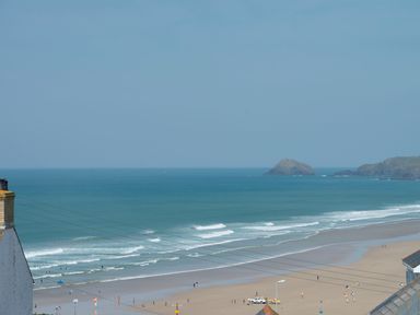 A beach with people on the sand and in the water and rocky islands in the distance at Spiral View in Perranporth