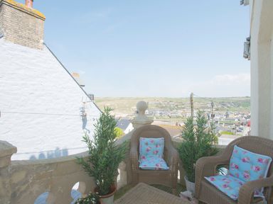 A small balcony with wicker chairs and plants overlooking a town at Spiral View in Perranporth