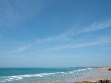 A wide sandy beach with waves and people near the shore at Spiral View in Perranporth