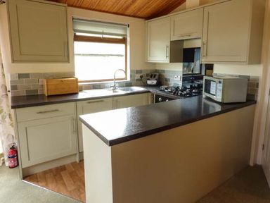 A kitchen with cabinets a countertop a gas stove a microwave a sink and a wooden breadbox at South Lodge in Kendal