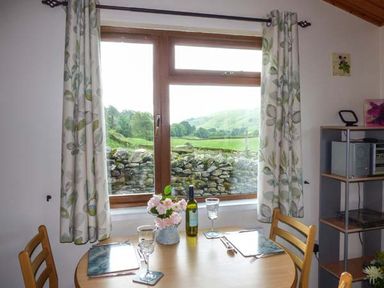 A dining table with chairs near a window with curtains showing a view of a stone wall and greenery at South Lodge in Kendal