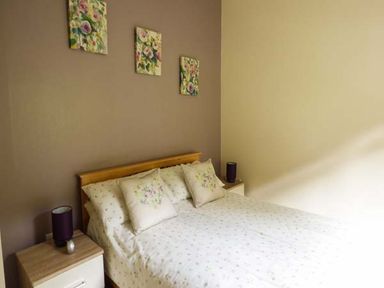 A bedroom with a bed flanked by two nightstands each with a lamp and three floral paintings on the wall at South Lodge in Kendal