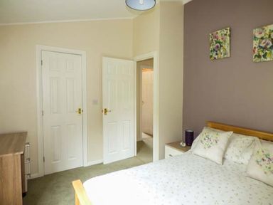 A bedroom with a double bed with floral pillows beside a wooden chest of drawers and two white doors at South Lodge in Kendal