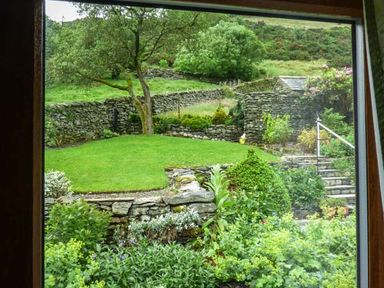 A garden with stone walls green grass bushes flowers and a tree seen through a window at South Lodge in Kendal