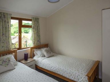A bedroom with two single wooden beds with floral bedding a nightstand with a lamp and floral curtains on a window at South Lodge in Kendal