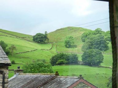 A view of green hills with trees and stone walls seen through a window at South Lodge in Kendal