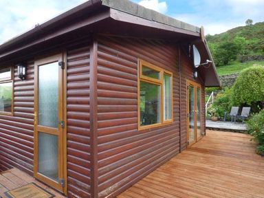 A wooden cabin exterior with glass doors and windows and a wooden deck at South Lodge in Kendal