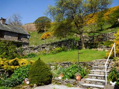 A garden with stone steps and stone walls near a stone house with trees and plants at South Lodge in Kendal