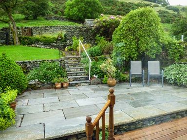 A stone patio with two chairs and steps leading to a garden with stone walls and greenery at South Lodge in Kendal