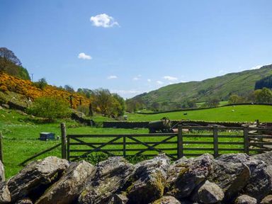 A rural landscape with green fields, a wooden gate, stone wall, and hills in the background at South Lodge in Kendal