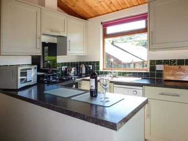 A kitchen with white cabinets black countertops a microwave a stove a sink and a window at North Lodge in Kendal
