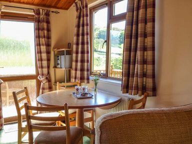 A dining area with a round wooden table and chairs near windows with checked curtains at North Lodge in Kendal