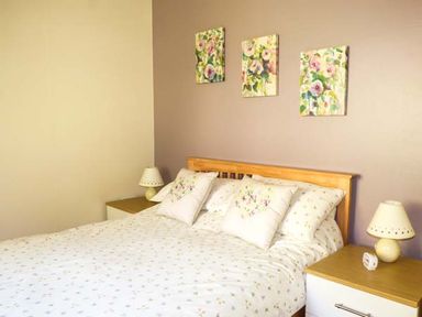 A bedroom with a wooden bed frame floral bedding and three floral paintings above the bed at North Lodge in Kendal