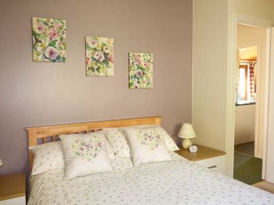 A bedroom with a wooden bed frame and floral bedding with pillows and a bedside table with a lamp and clock at North Lodge in Kendal