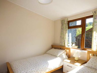 A bedroom with two single beds a nightstand and a window with curtains at North Lodge in Kendal