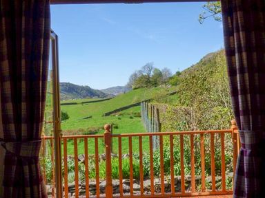 A wooden balcony with railing looking out to a green hillside and blue sky at North Lodge in Kendal