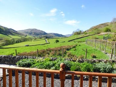 A countryside view with green fields hills and stone fences seen from behind a wooden railing at North Lodge in Kendal
