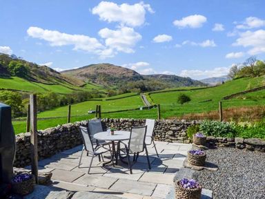 An outdoor patio with a round table and four chairs surrounded by a stone wall with green fields and hills in the background at North Lodge in Kendal