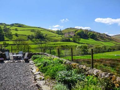 An outdoor seating area with a table and chairs overlooking green hills and fields at North Lodge in Kendal