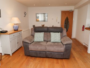 A living room with a gray sofa two cushions wooden floor mirror sideboard and a door at 6 Mill Wharf in Berwick-upon-Tweed