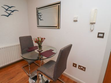 A small dining area with a round glass table two grey chairs a vase with flowers wall mirror and wall-mounted telephone at 6 Mill Wharf in Berwick-upon-Tweed