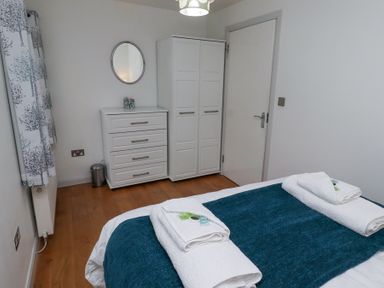 A bedroom with a bed covered in blue and white linens a white wardrobe a chest of drawers with a mirror above at 6 Mill Wharf in Berwick-upon-Tweed
