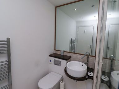 A bathroom with a wall-mounted round sink a toilet a large mirror and a towel radiator at 6 Mill Wharf in Berwick-upon-Tweed