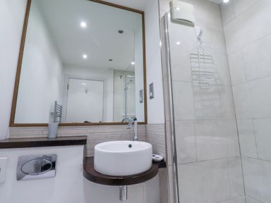 A bathroom with a round sink on a wooden countertop a large mirror and a glass shower enclosure at 6 Mill Wharf in Berwick-upon-Tweed