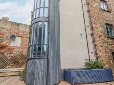 An outdoor area with stone walls wooden decking large curved windows and blue wooden fencing at 6 Mill Wharf in Berwick-upon-Tweed