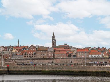 A waterfront view of a town with old buildings and a clock tower at 6 Mill Wharf in Berwick-upon-Tweed