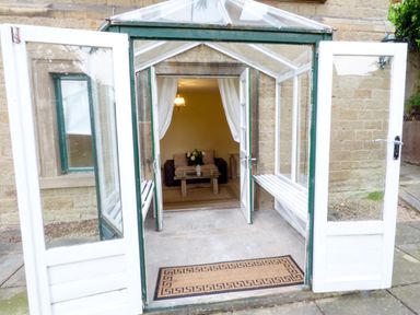 An open glass porch with benches leading to a living room with a sofa and coffee table at Garden View in Malvern