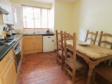 A kitchen with wooden cabinets a dining table with chairs and kitchen appliances at Garden View in Malvern