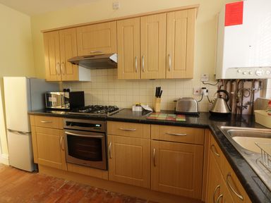 A kitchen with wooden cabinets a gas stove oven fridge microwave kettle toaster and a sink at Garden View in Malvern