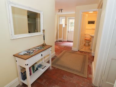 A hallway with a white table holding books and brochures a mirror on the wall a beige rug a door leading to a bathroom and an exit door at Garden View in Malvern