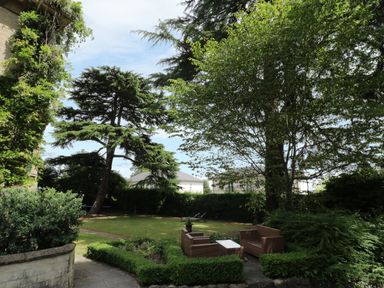 A garden with patio furniture including a sofa and armchairs surrounded by trees and hedges at Garden View in Malvern