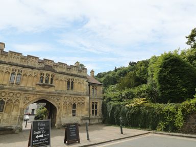 A stone building with an arched entrance and signs outside next to a wall covered with greenery and trees in the background at Garden View in Malvern