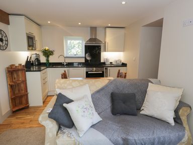 A living room with a sofa and cushions open to a kitchen with white cabinets and appliances at The Granary Loft in Bardsea