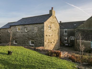 A stone cottage with grass lawn and small trees outside at The Granary Loft in Bardsea