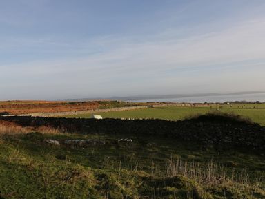 A grassy field with stone walls and some sheep in the distance at The Granary Loft in Bardsea