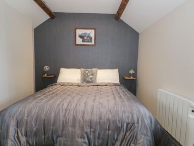 A bedroom with a double bed a gray bedspread two white pillows a decorative cushion two wall lamps and a framed picture of a cow at The Granary Loft in Bardsea
